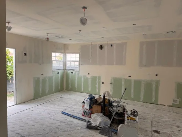 Interior of a room under construction or renovation with drywall, unpainted walls, and construction tools and supplies on the floor.