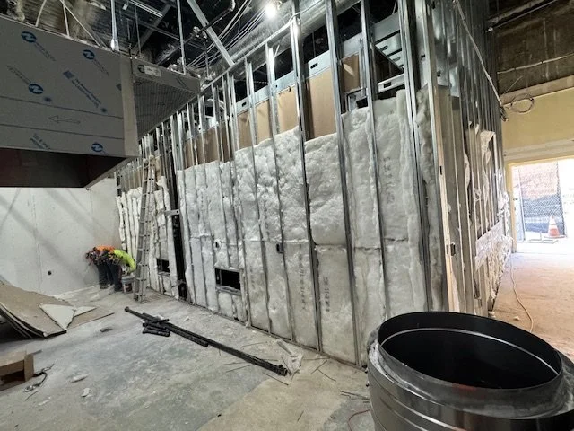 Construction site with metal framing and insulation being installed on a wall, ladder, and construction tools.