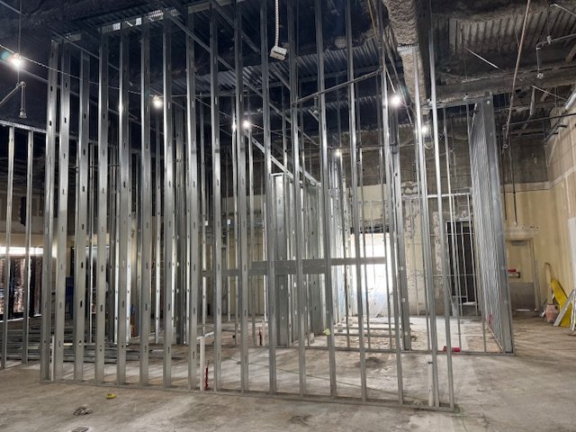 Interior view of a building under construction with metal framing walls and exposed ceiling with wiring.