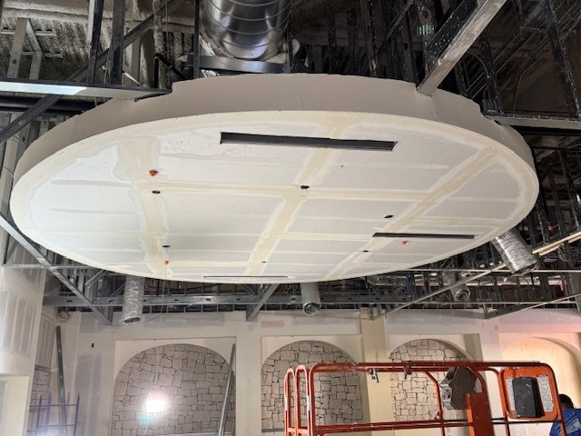 Large circular ceiling panel installed in an industrial or commercial building interior, with exposed ductwork and metal framework.