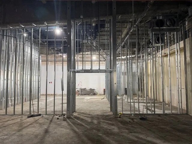Interior of a building under construction with exposed metal framing and electrical wiring, no finishes installed yet.
