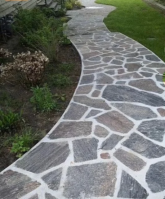 Curved stone pathway with irregular gray stones bordered by green grass and garden plants.