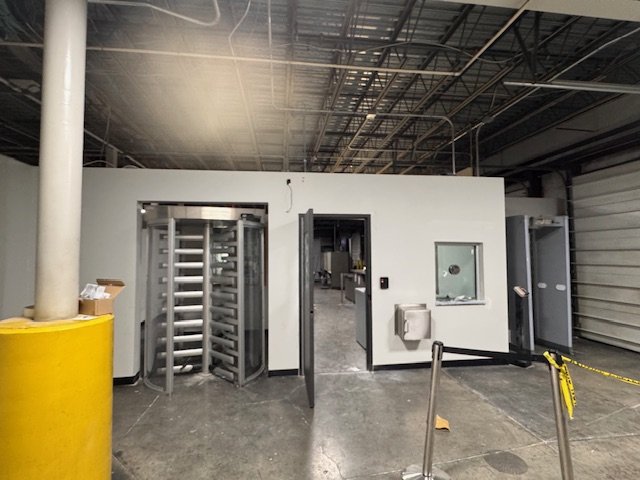 Interior of a secured facility with turnstiles and a door leading to another room, industrial garage setting.