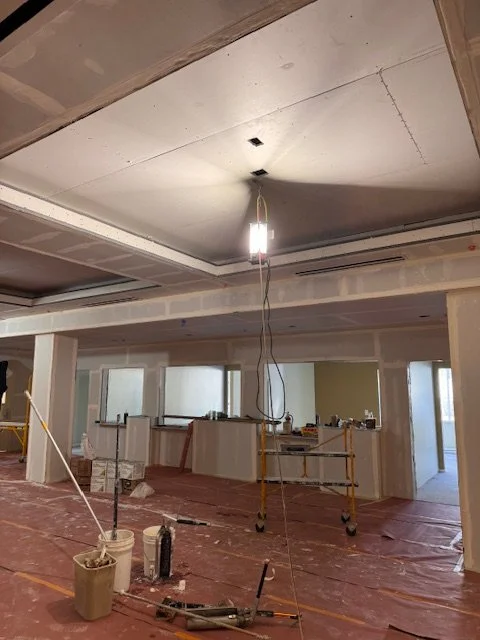 Construction site with a ceiling being installed, hanging light fixture in the center, and construction tools on the floor.
