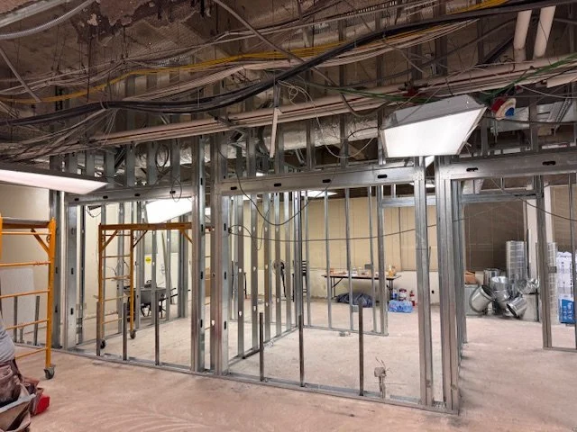 Construction site with exposed metal framing and electrical wiring, partially built interior walls, and construction equipment.