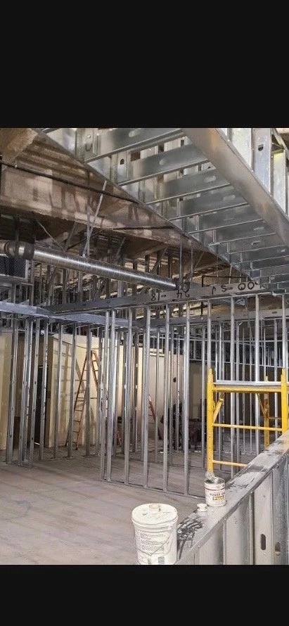 Interior view of a building under construction with metal framing, scaffolding, and construction tools.