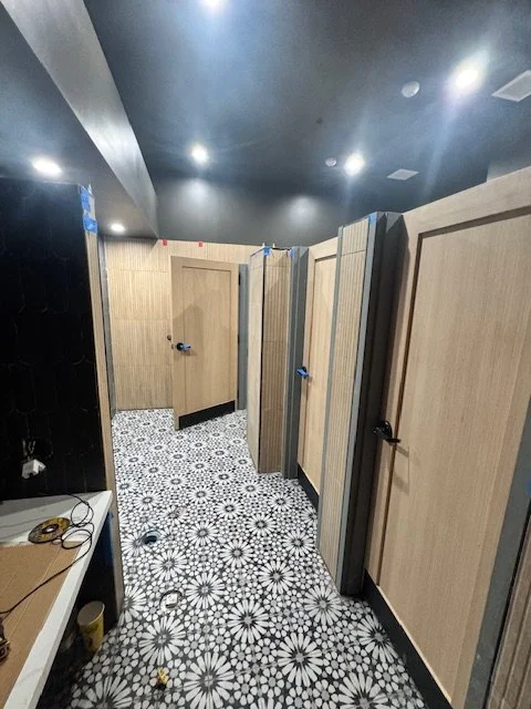 Public restroom with multiple stall doors, patterned tile floor, and black ceiling.