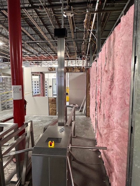 Construction site with steel framing, pink insulation on wall, and a turnstile gate in the foreground.