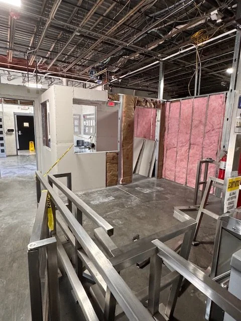 Construction site with exposed framing, pink insulation, and metal barriers, indicating ongoing building or renovation.