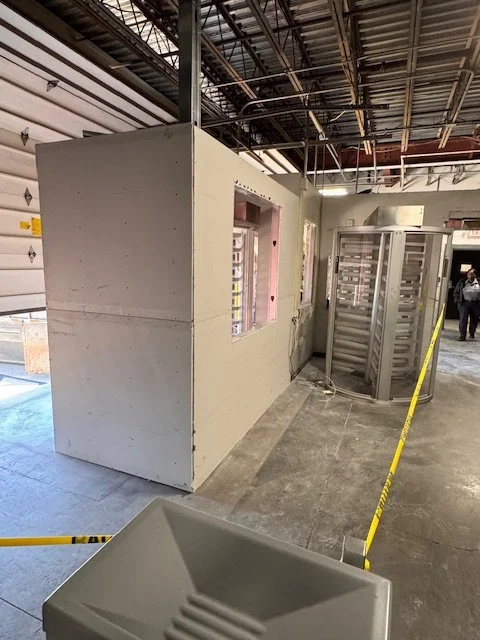 Interior of a construction site with drywall walls, a temporary window frame, a white electrical enclosure, and yellow caution tape.
