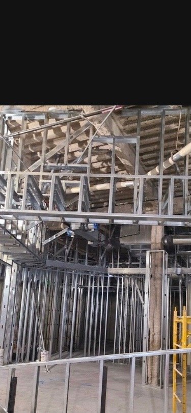 Construction site with metal framing and scaffolding, with some pipes and wooden beams visible in the background.