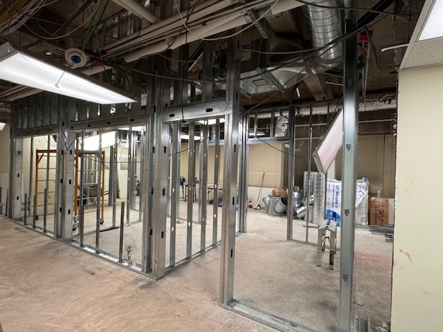 Construction of an indoor space with exposed metal framing for walls and ceiling, and construction materials scattered around.