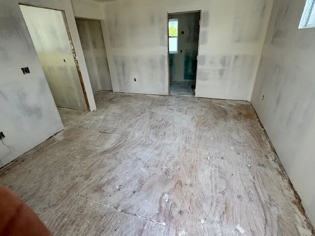 Empty room with drywall walls and exposed floor, no furniture or decorations, appears to be under construction or renovation.