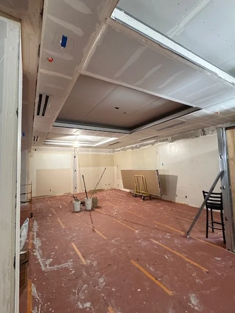 Room under construction with unfinished drywall, exposed ceiling, and construction materials on the floor.