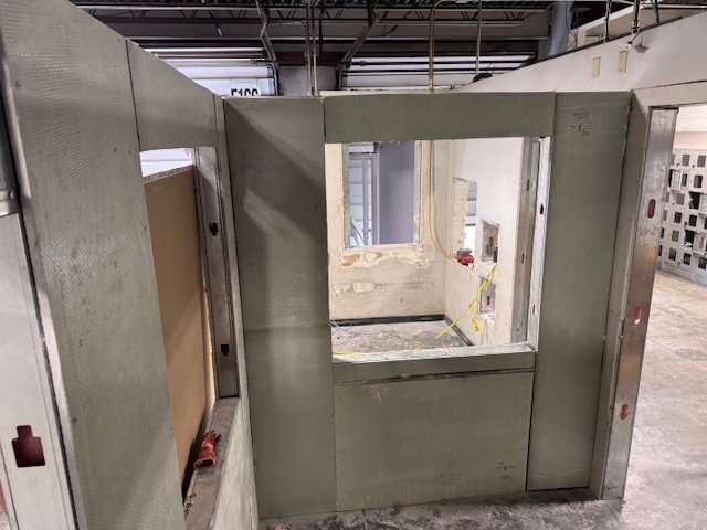 Empty armored vehicle or shipping container with windows and interior panels, in an industrial setting.