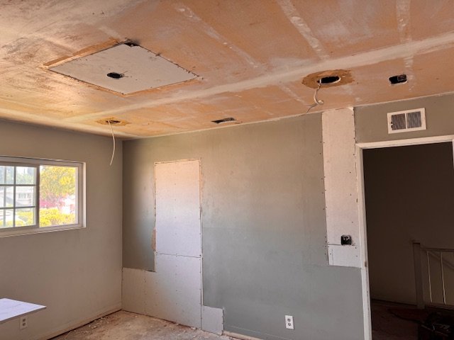 Room under renovation with unfinished ceiling, one window, and a partially covered wall.
