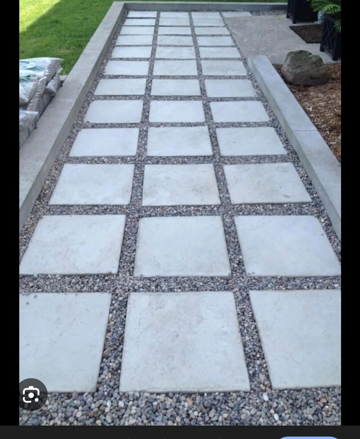 A newly laid stone pathway with large square white stones bordered by smaller pebbles, set in a grid pattern in a garden area.