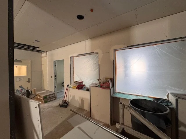 Construction site with unfinished walls and windows covered with plastic sheeting, construction tools, and equipment scattered around.