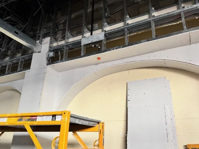Construction site with scaffolding, a yellow ladder, and an unfinished wall in a building interior.