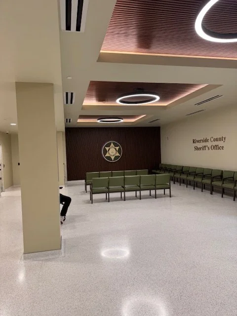 Interior of Riverside County Sheriffs Office waiting area with green chairs and a wall with sheriff badge and sign.
