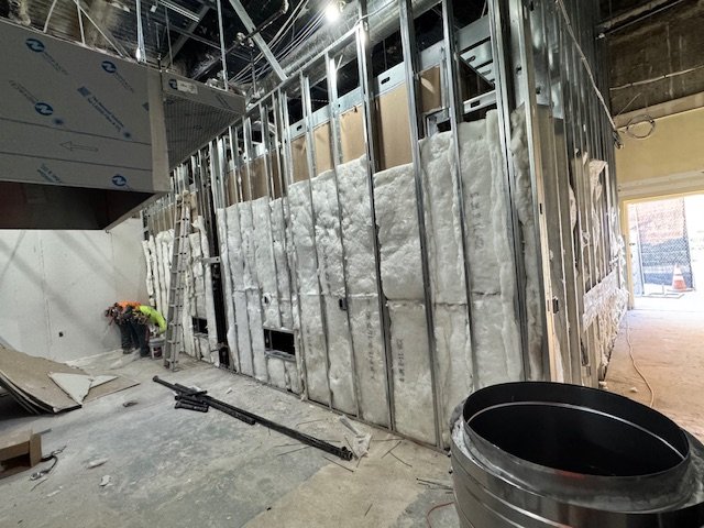 Construction site with metal framing, insulation, and tools, indicating ongoing building work.