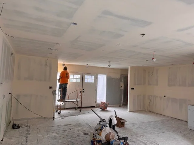 Person working on ceiling in a room under renovation, with construction materials and tools on the floor.