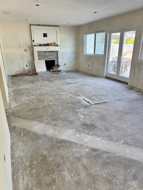 Empty living room under renovation with concrete floor, unfinished walls, a fireplace, and large windows and sliding glass door leading outside.