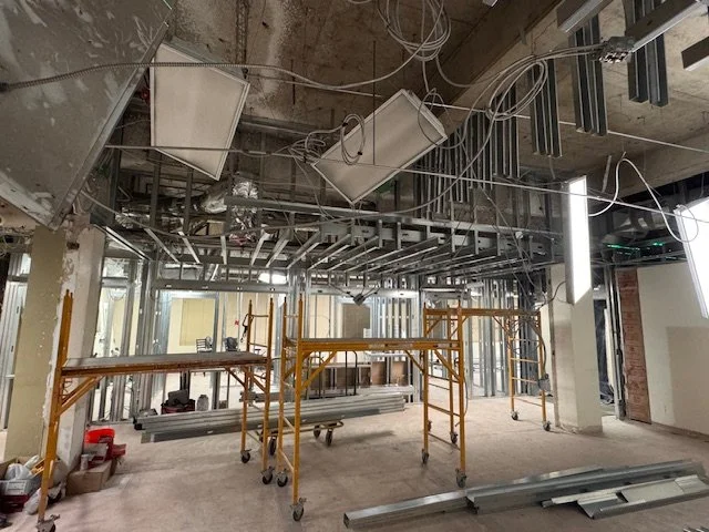 Construction site with exposed ceiling infrastructure, scaffolding, and metal framing inside a building under renovation.