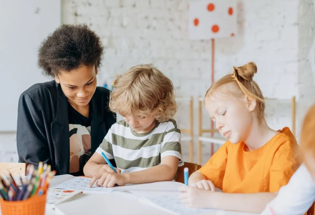 A teacher helping two young children with their schoolwork in a classroom.
