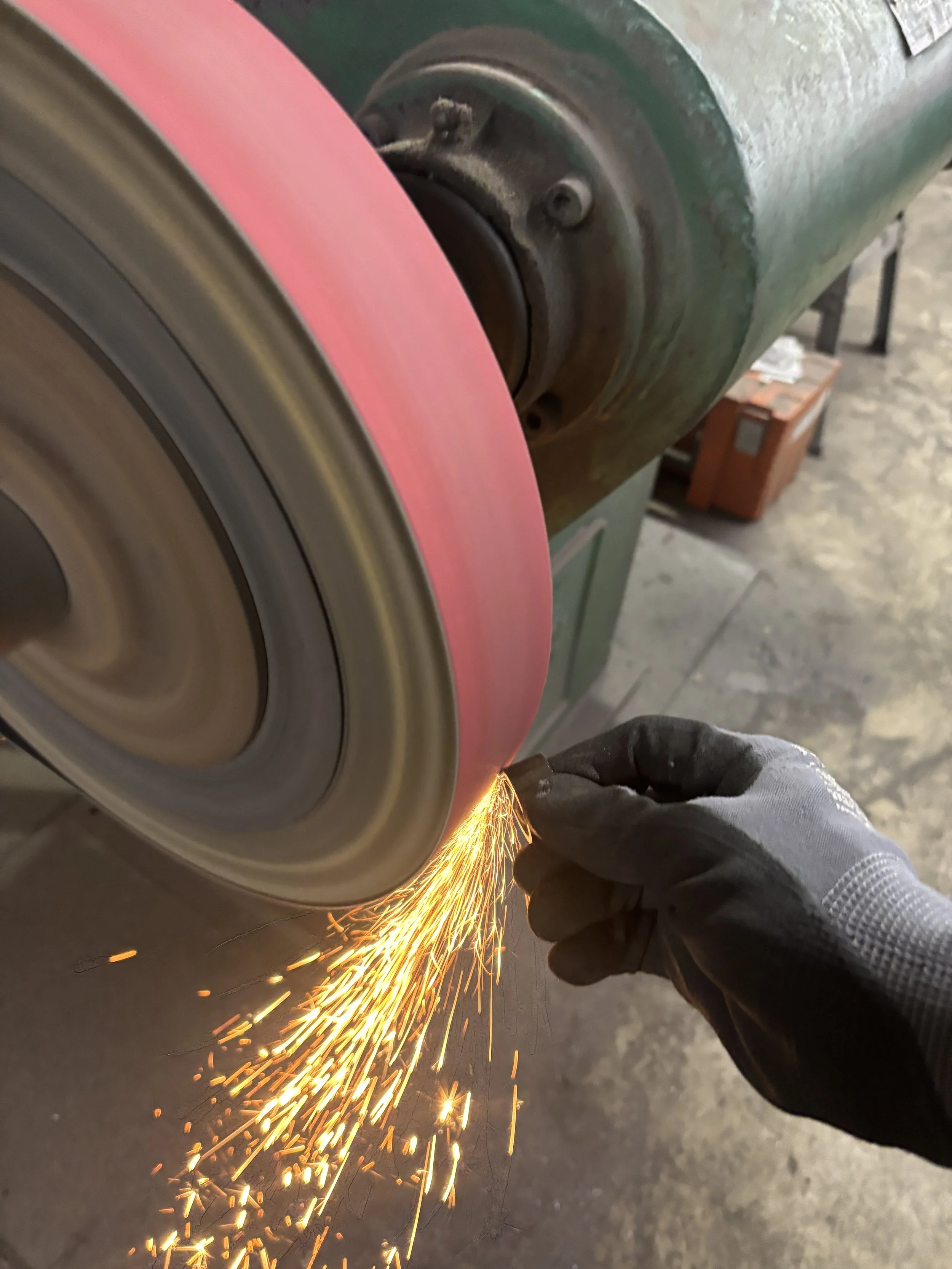 A worker wearing protective gloves grinding with an angle grinder, causing bright sparks to fly off on a metal surface.