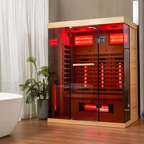A modern infrared sauna with glass doors inside a room with wooden flooring and a potted plant nearby.