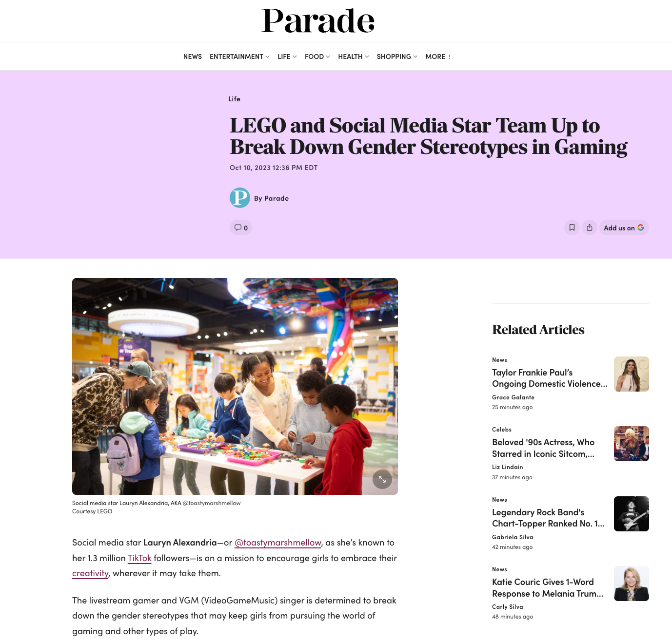 People, including children and adults, gathered around a table at an indoor event, engaging with LEGO pieces and socializing, with colorful decorations and a rainbow sculpture in the background.