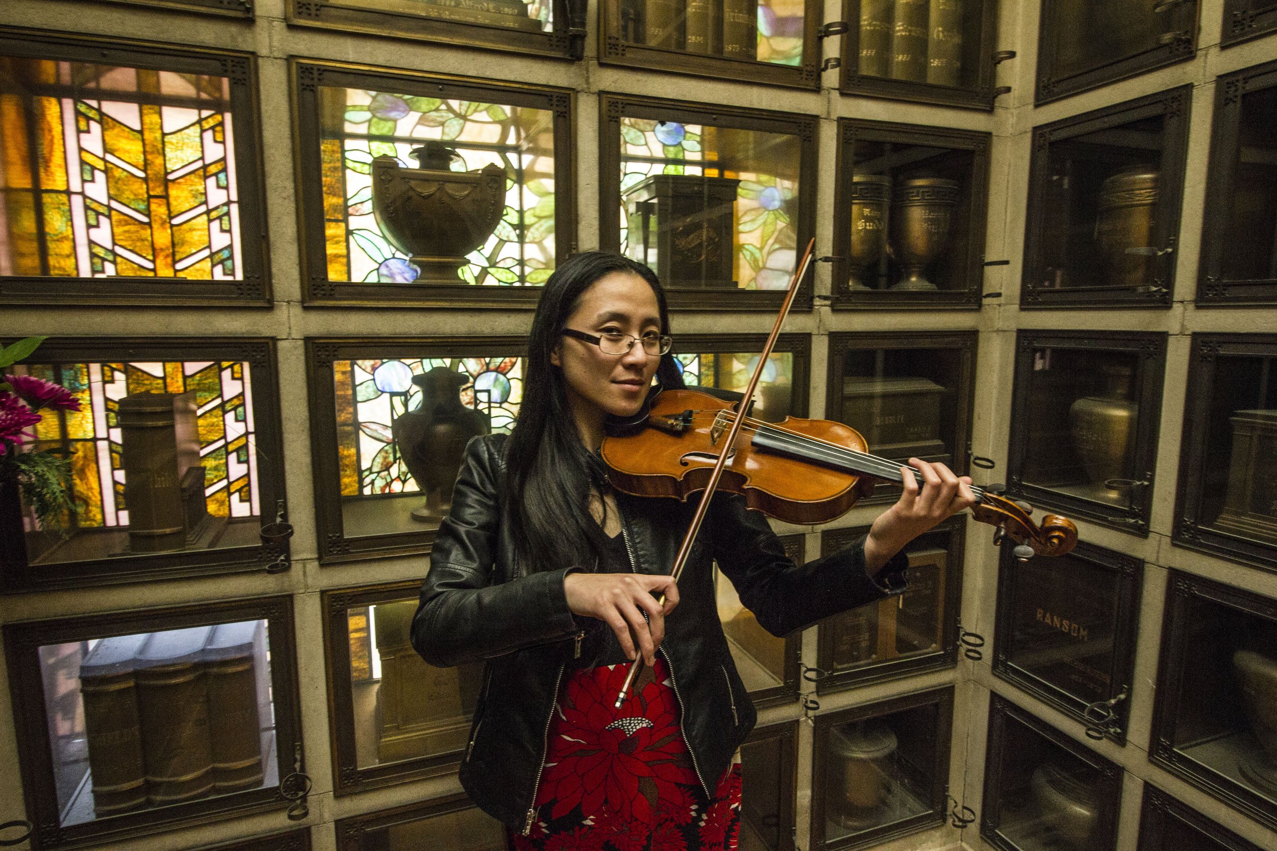 Woman playing violin in front of stained-glass windows and display cases