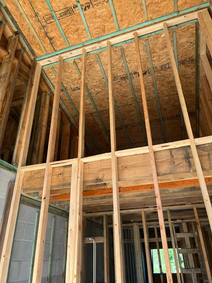 Interior view of a building under construction with exposed wooden framing and plywood ceiling.