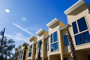 Row of modern townhouses with large glass windows and balconies under a clear blue sky with a few clouds.