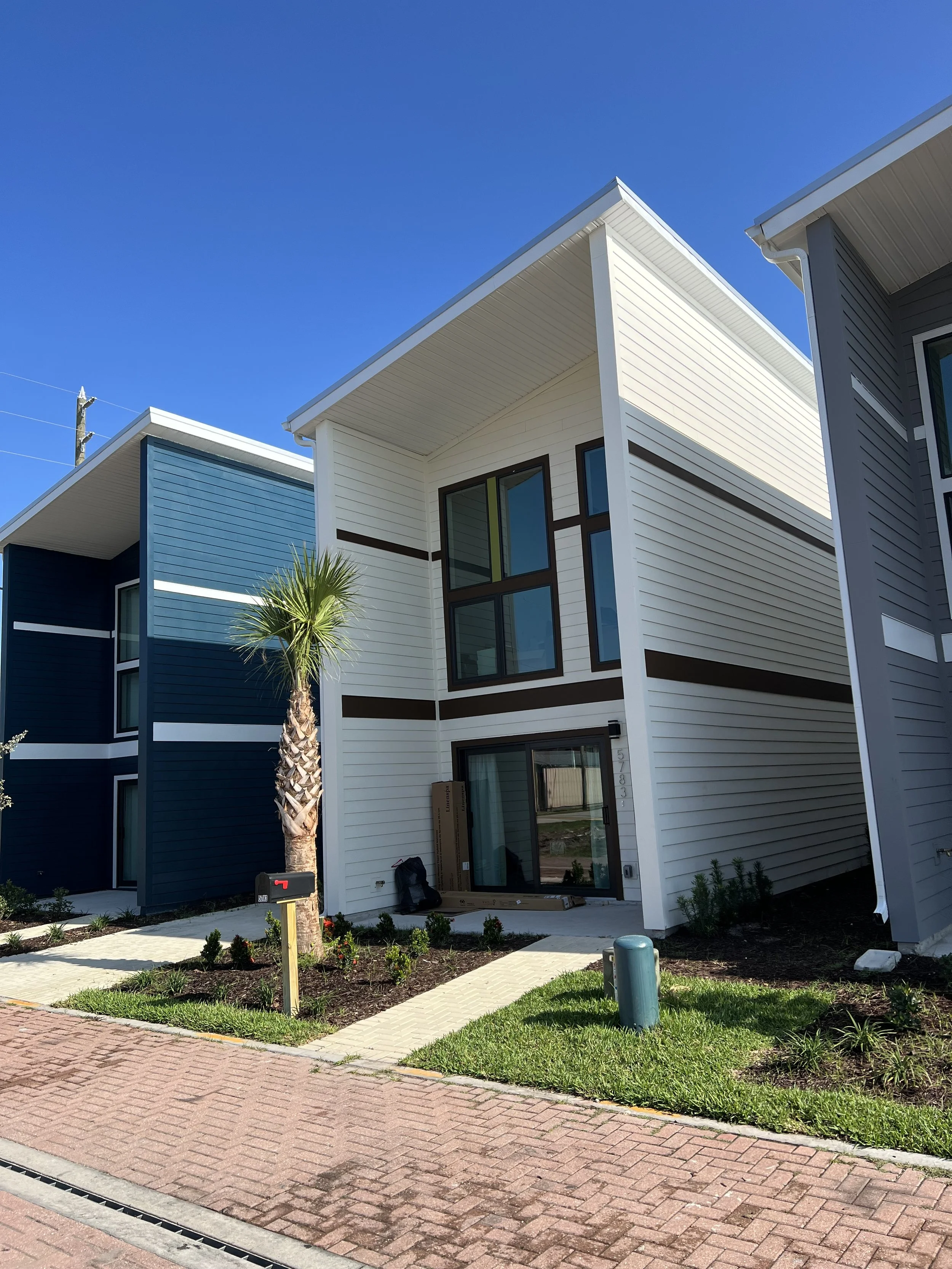 New modern multi-story house with white and blue siding, large windows, and a landscaped front yard under a clear blue sky.