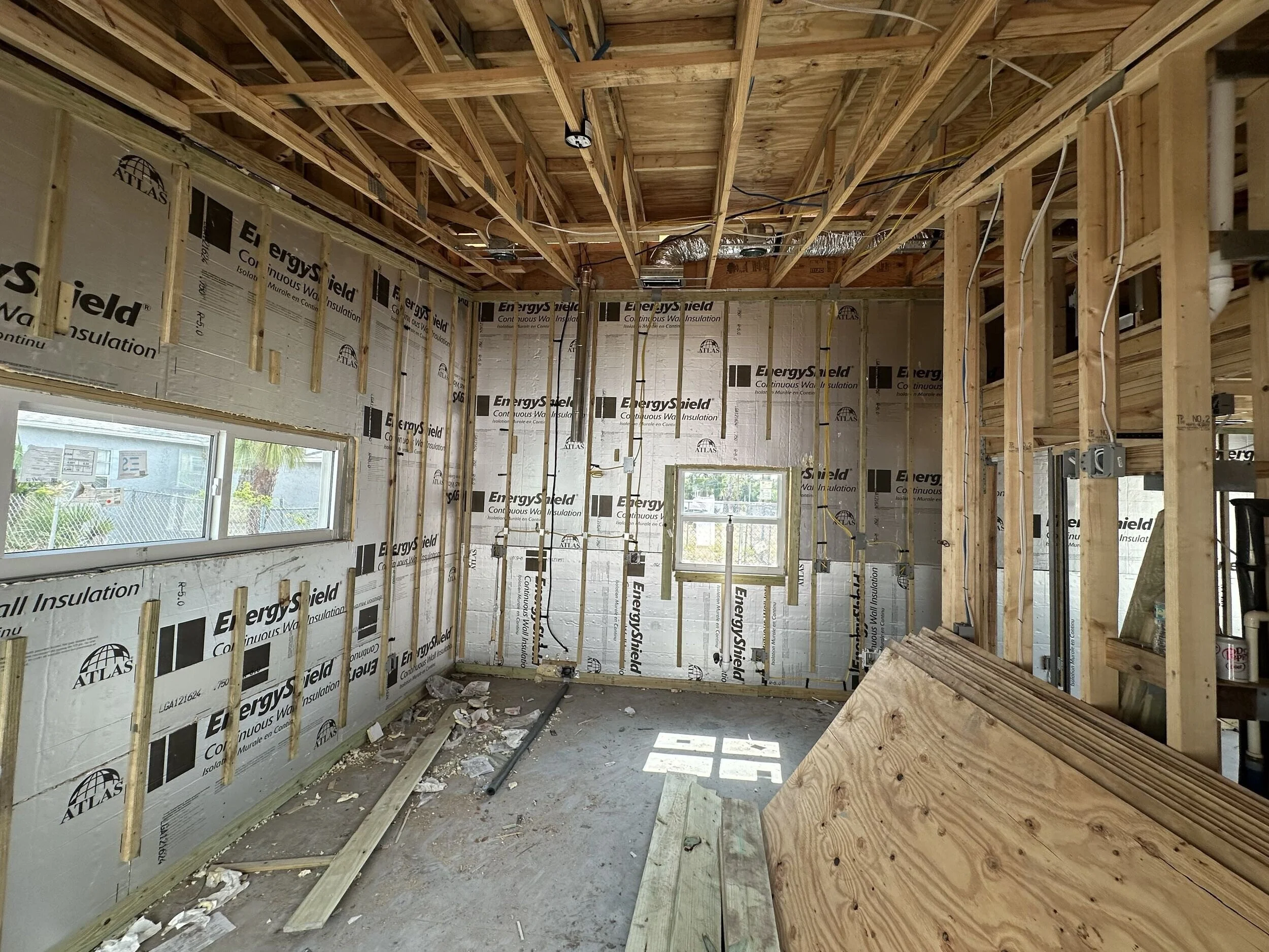 Interior view of a house under construction with exposed wooden framing and insulation on the walls.