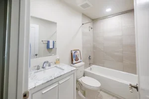 Bathroom with white vanity, mirror, toilet, and bathtub with shower, beige tiles, and white walls.