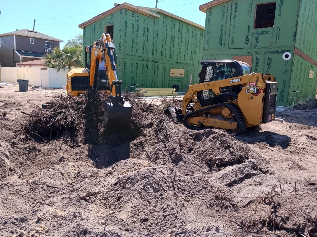 Construction site with two small yellow excavators digging up dirt in front of a green building under construction