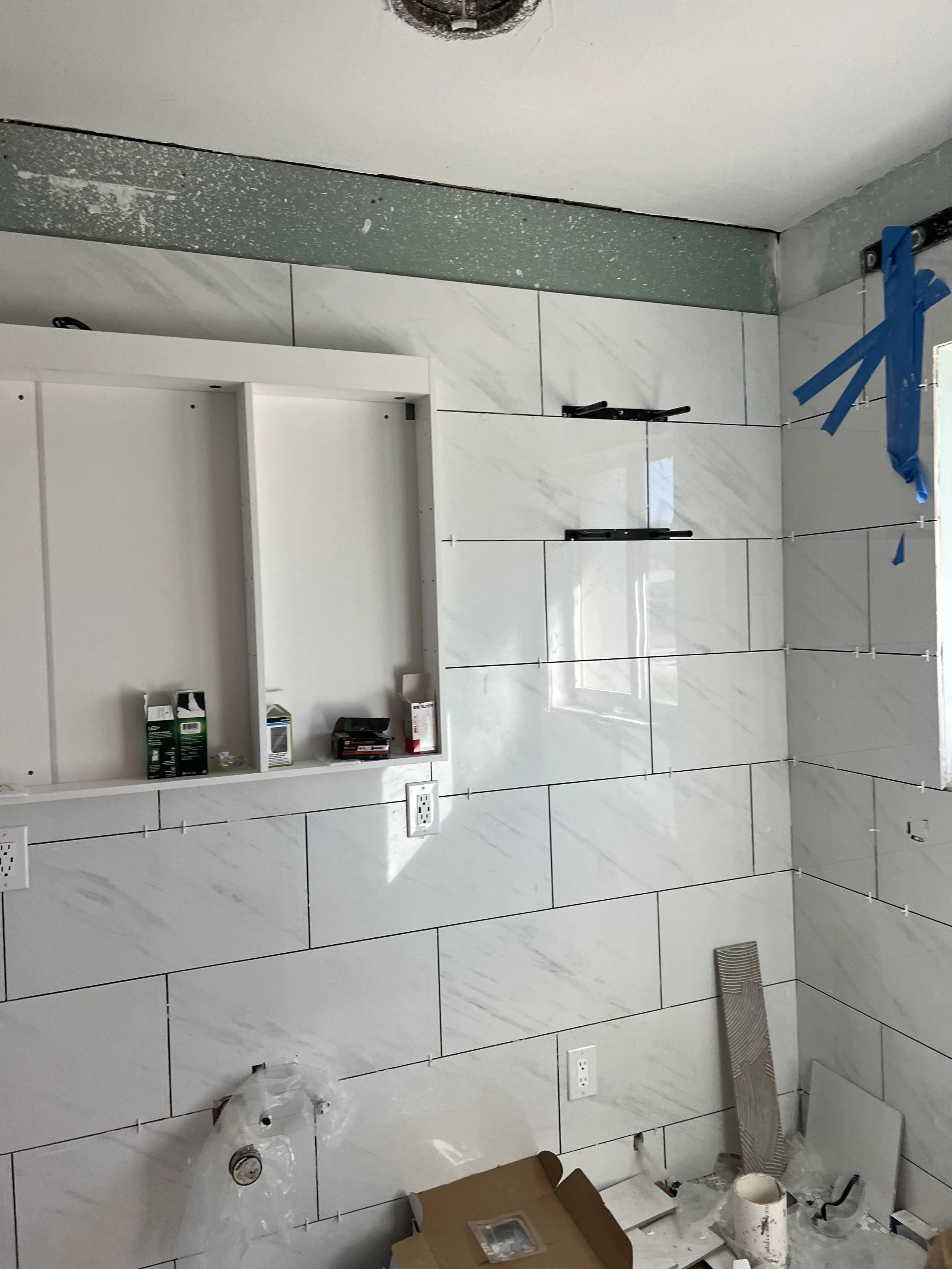 A bathroom under renovation with partially tiled wall, construction tools, and supplies scattered around.