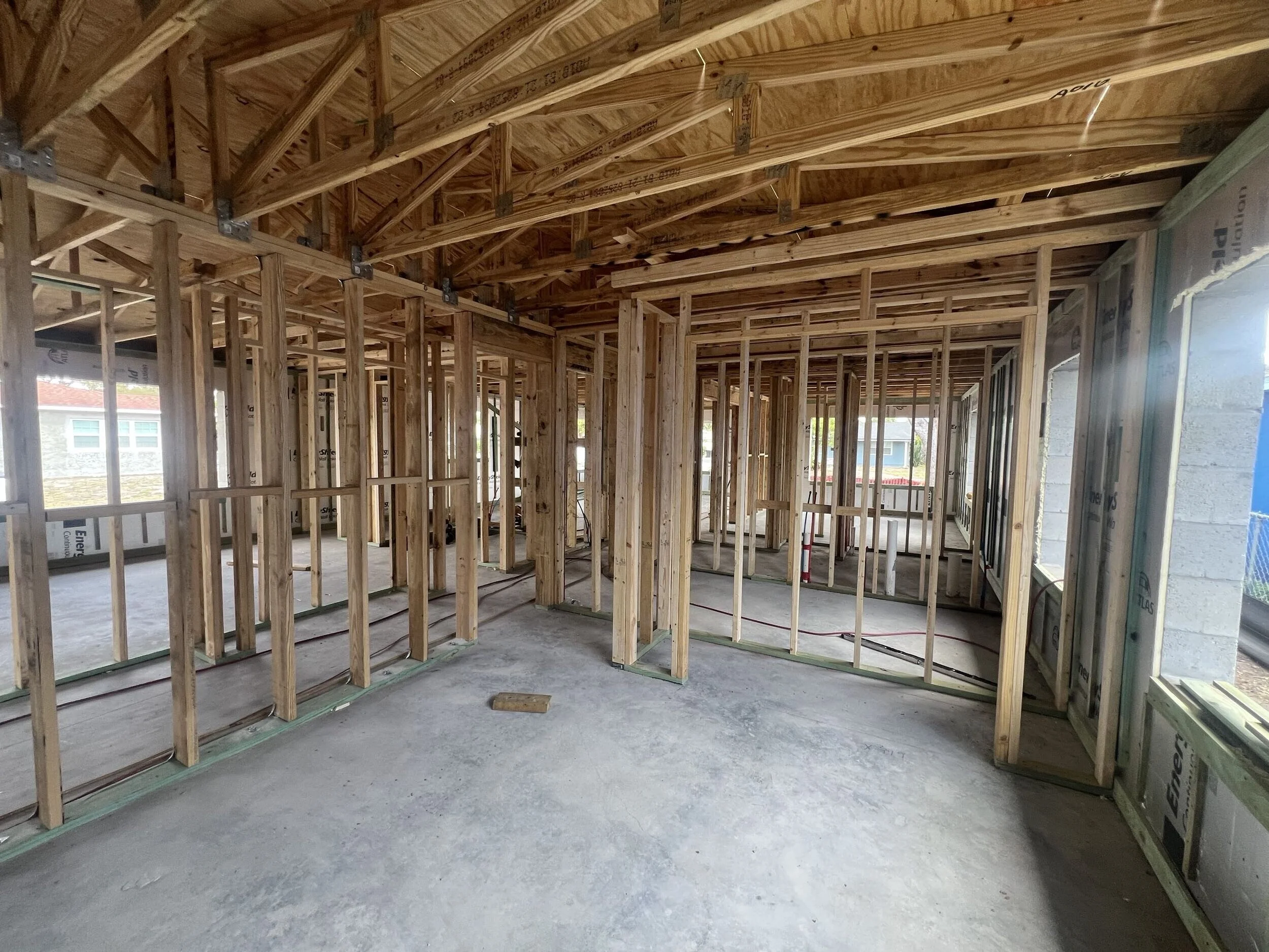 Interior view of a house under construction with exposed wooden framing, studs, and ceiling joists.