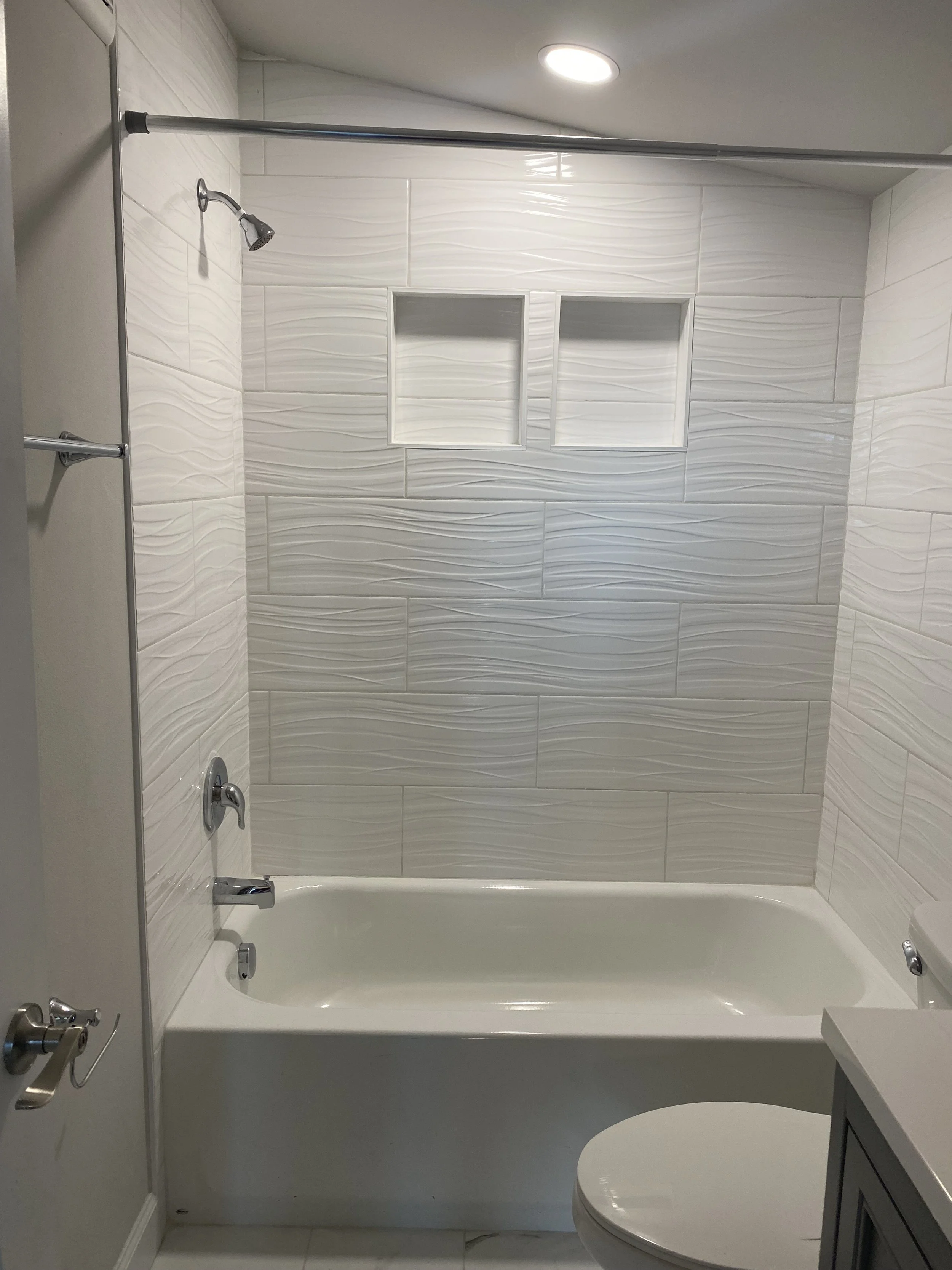 Bathroom with a bathtub, showerhead, and built-in wall shelves, white tiles, and a gray vanity cabinet.