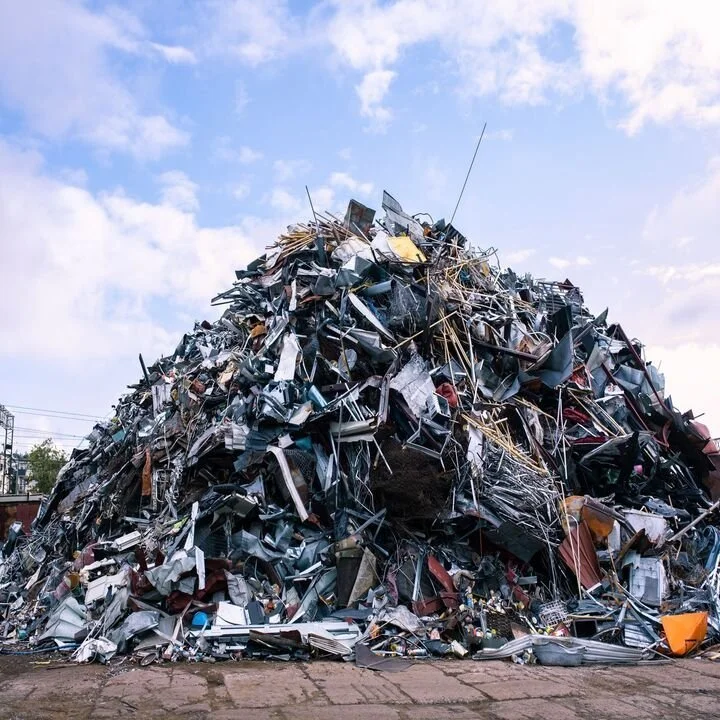Pyramid of assorted scrap metal and discarded items outside against a cloudy sky.