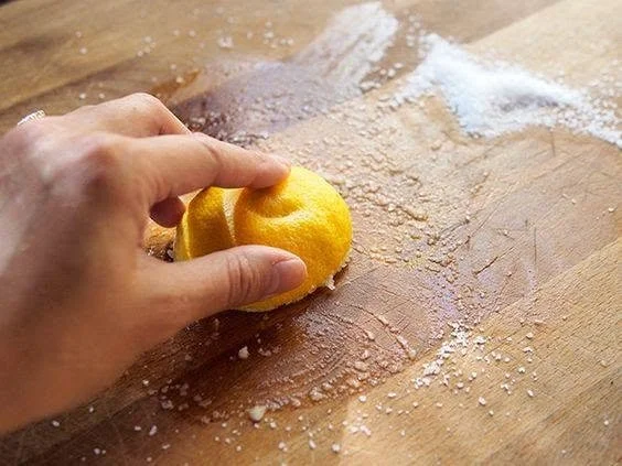 Close-up of a hand holding a yellow lemon over a floured wooden surface.