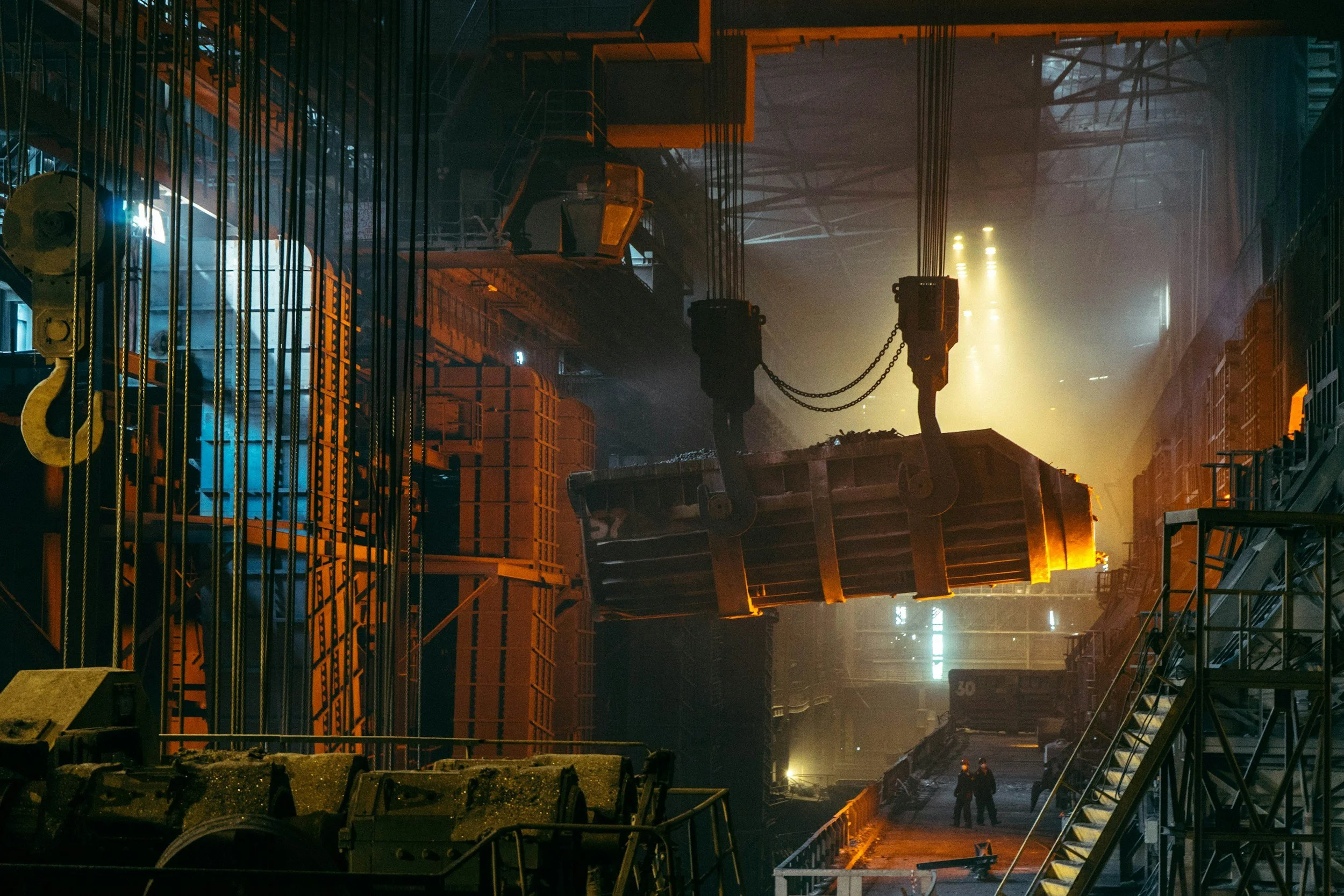 A large industrial factory or warehouse with machinery, cables, and metal structures. Bright light sources create a hazy atmosphere with orange and blue hues.