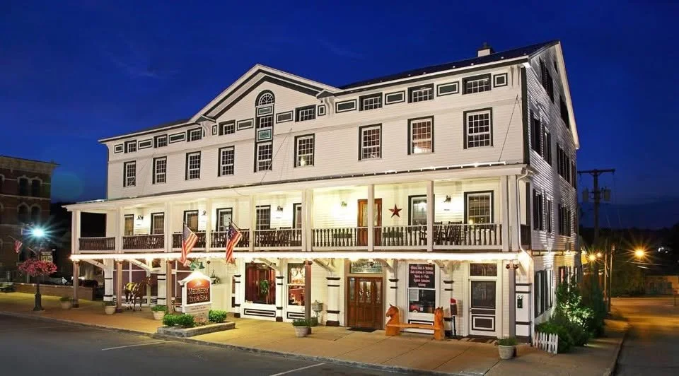 Large white multi-story building with balconies, decorated with flags and outdoor seating, illuminated at night.