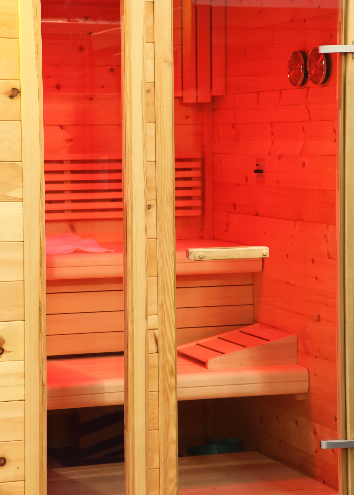 Wooden infrared sauna with glass door and side panel, situated in a room with yellow wall and wood ceiling.