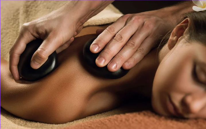 Person receiving a hot stone massage on their back with smooth, black stones.