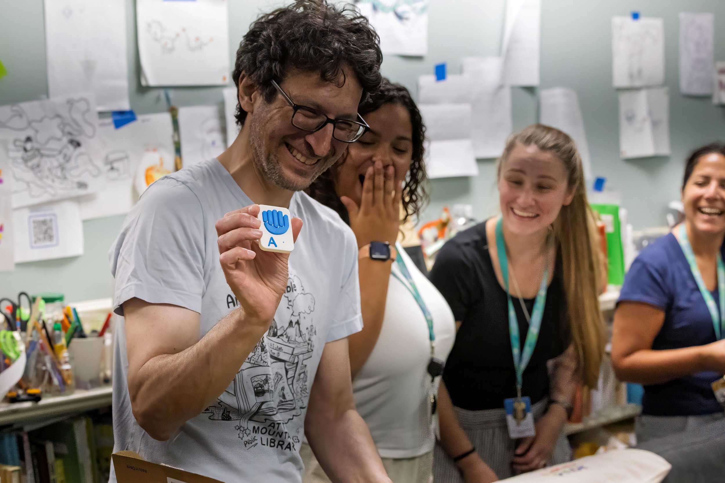 ML Makerspace Director Ian Matty holding up a 3D-printed tile that shows the American Sign Language letter 'A', standing alongside our collaborators from Sound Start Babies. Photo © James Maione