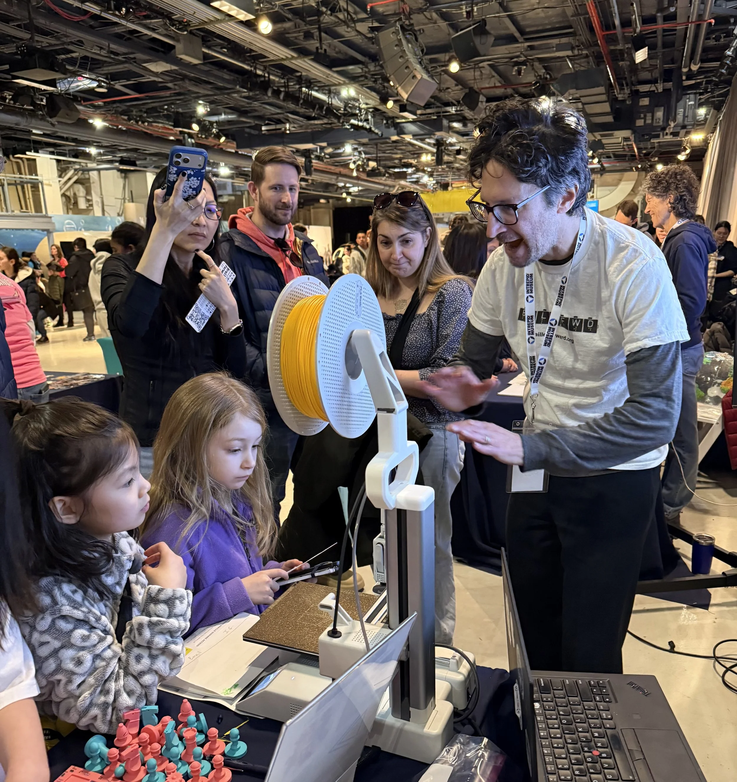 Ian Matty explains a 3D-printing life demonstration to a crowd at a tabling event.